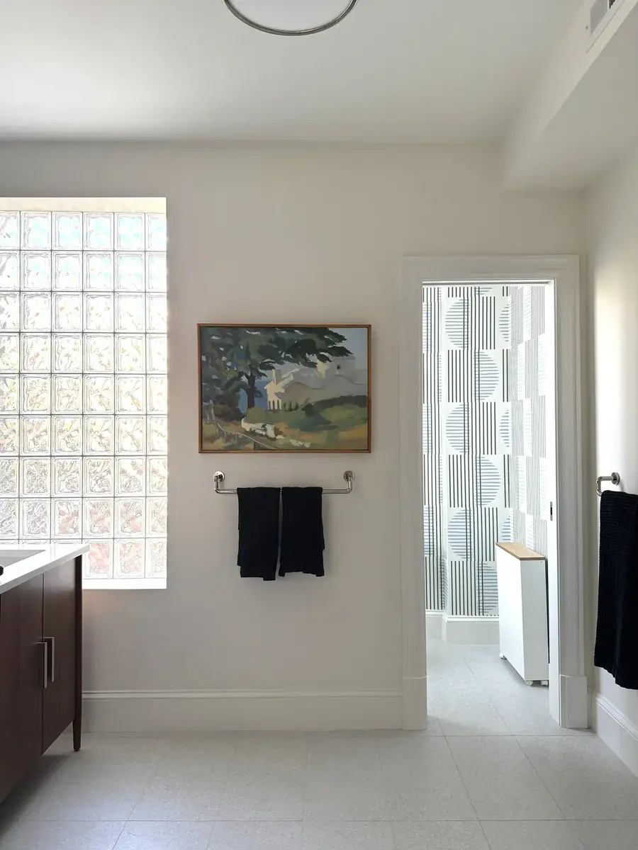 A complete primary bathroom remodel in NW Washington, DC highlighting white tile flooring, a glass block window, dark wood vanity, and a pocket door into the toilet area.