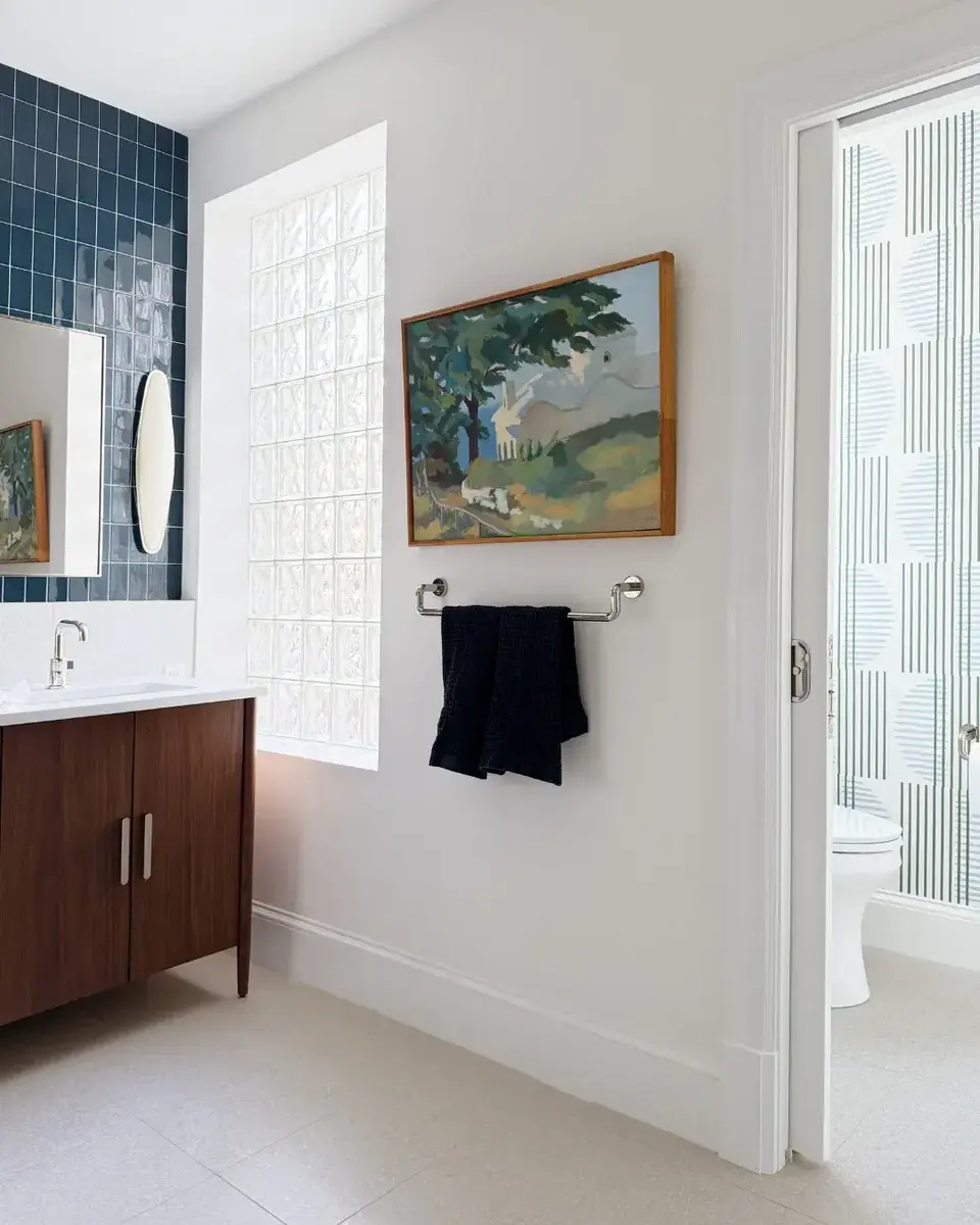 After photo of a primary bathroom remodel in NW Washington, DC featuring a walnut vanity, white tile flooring, glass block window, and a pocket door separating the toilet area.