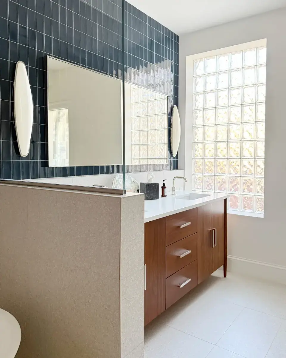 Remodeled primary bathroom in NW Washington, DC with dark blue-green tiled accent walls, frameless shower glass, walnut double vanity, and glass block window.