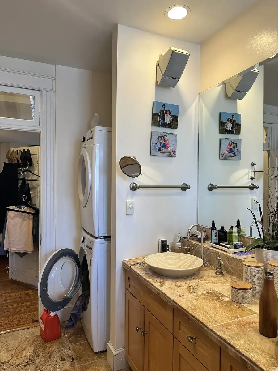 Before photo of a primary bathroom and laundry room remodel in NW Washington, DC showing a stacked washer and dryer beside an older wood vanity and sink.