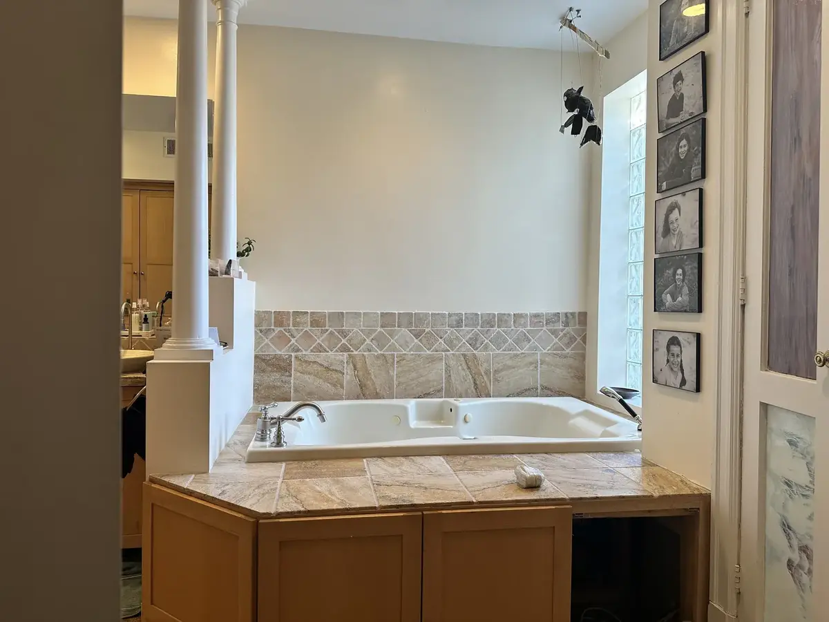 Before photo of a complete primary bathroom remodel in NW Washington, DC featuring an older built-in jetted bathtub, beige tile surround, and wood cabinets.