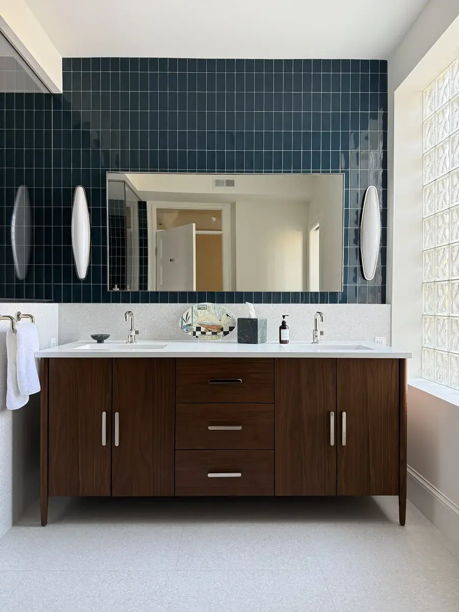 Renovated primary bathroom in NW Washington, DC with a floating-style walnut double vanity, vessel-like wall lighting, and deep blue-green tiled accent wall.