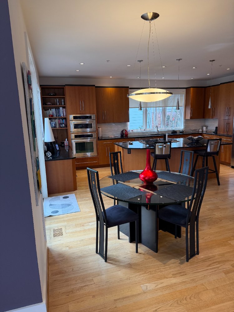 Open dining area and custom kitchen in Chevy Chase, MD featuring wood cabinetry and a glass dining table.
