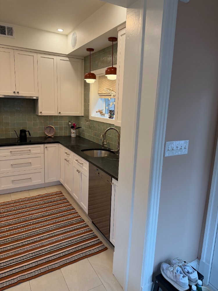 Corner view of a custom kitchen remodel featuring black countertops, white shaker cabinets, and pendant lighting.