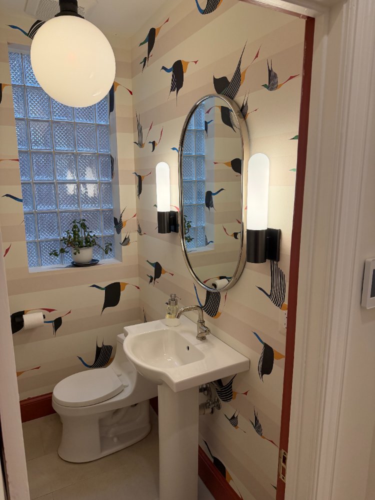 Powder room remodel featuring decorative wallpaper, pedestal sink, and modern wall sconces in Northwest Washington, D.C.