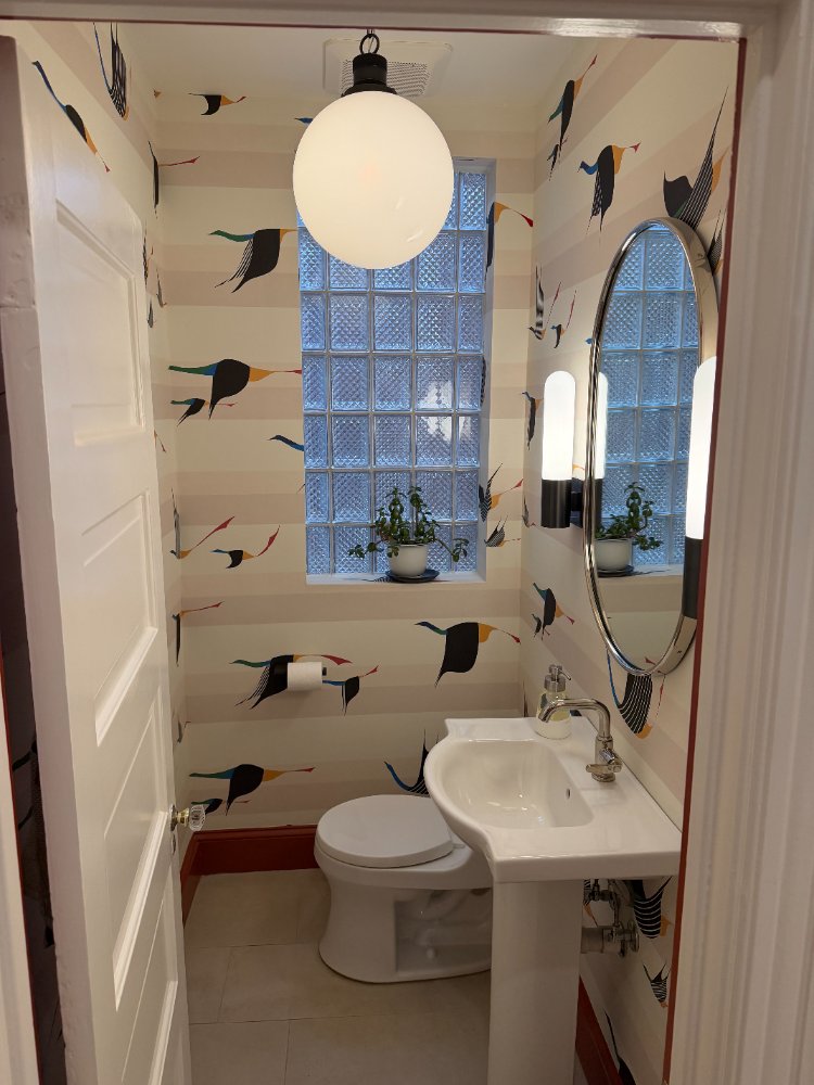 Stylish powder room remodeled with designer wallpaper, pedestal sink, and oval mirror in Northwest Washington, D.C.