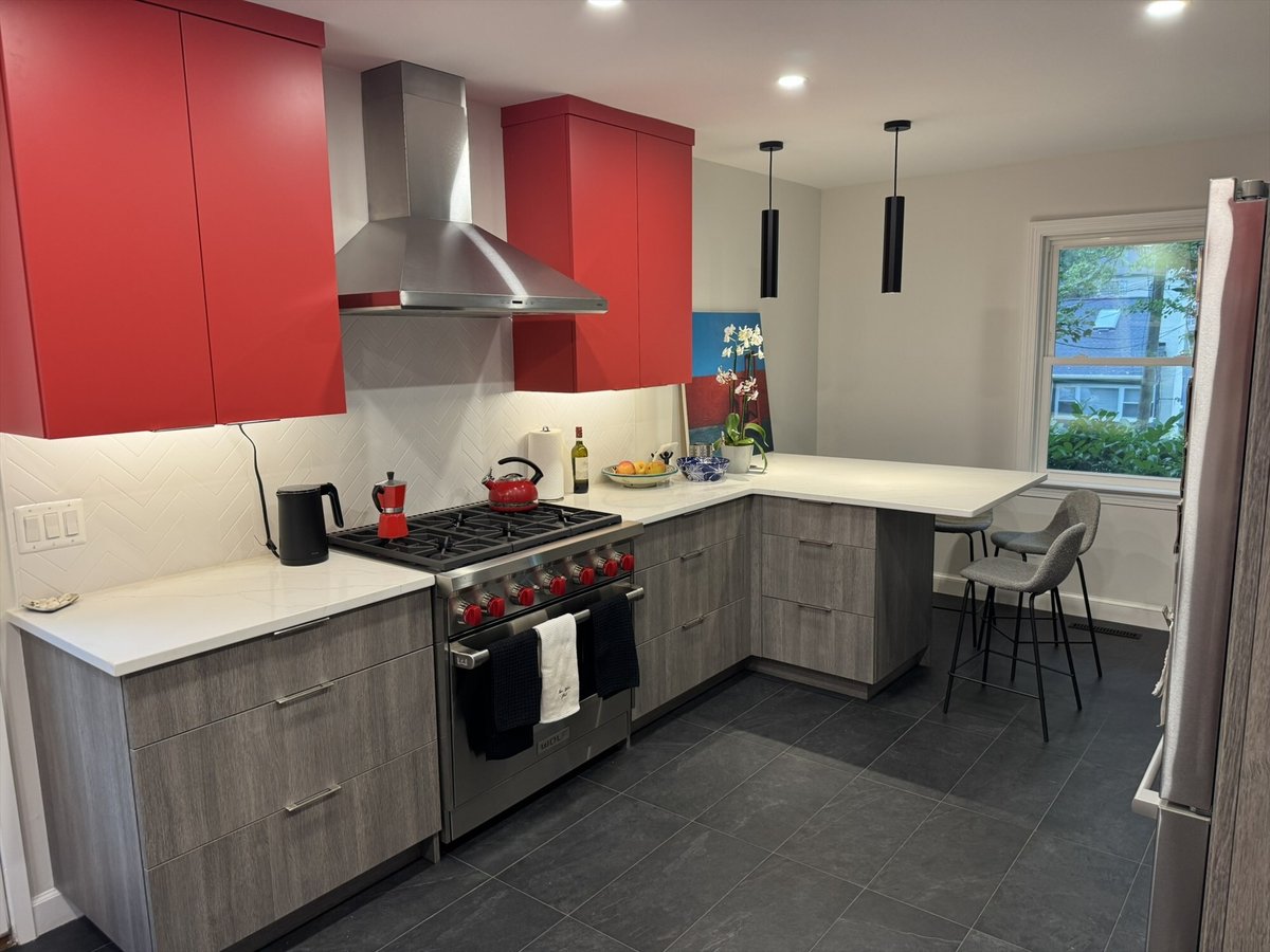 Modern L-shaped kitchen with red upper cabinets, a Wolf range, stainless steel hood, and a quartz peninsula in Chevy Chase, MD -