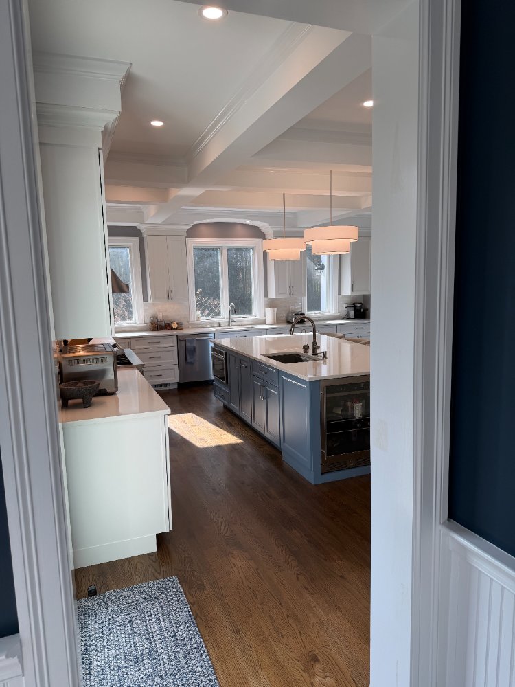 View into a remodeled kitchen with a blue island, coffered ceiling, and quartz countertops in Chevy Chase, MD.