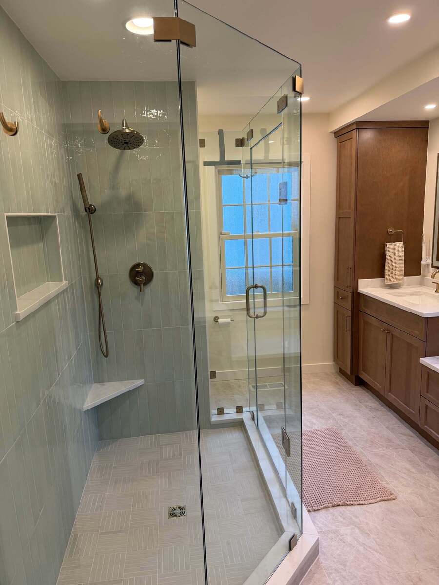 Primary bathroom remodel in Potomac, MD featuring a frameless glass walk-in shower, sage green vertical wall tiles, brushed brass fixtures, and a custom wood vanity.