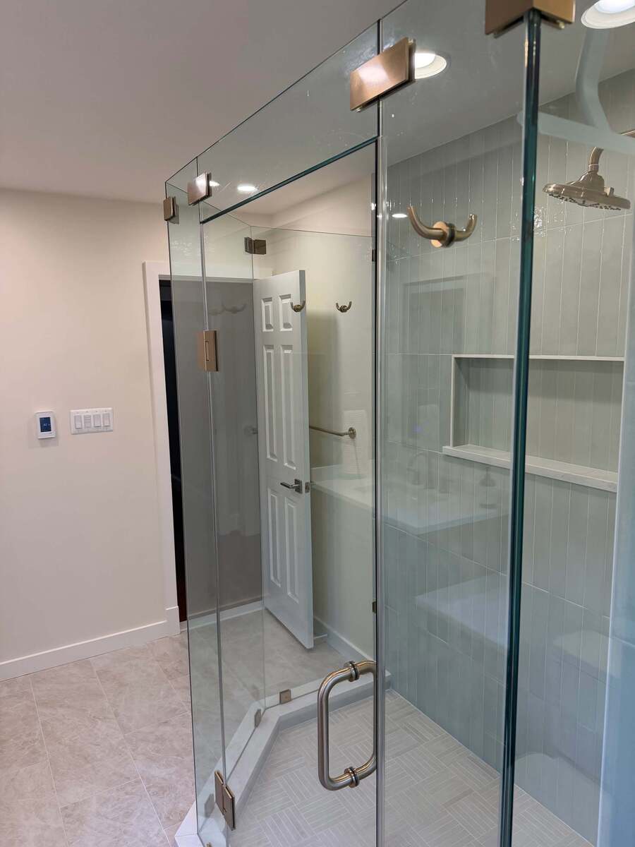 Frameless glass walk-in shower in a Potomac, MD primary bathroom remodel featuring sage green vertical tile, built-in shower niches, brass hardware, and a rainfall showerhead.