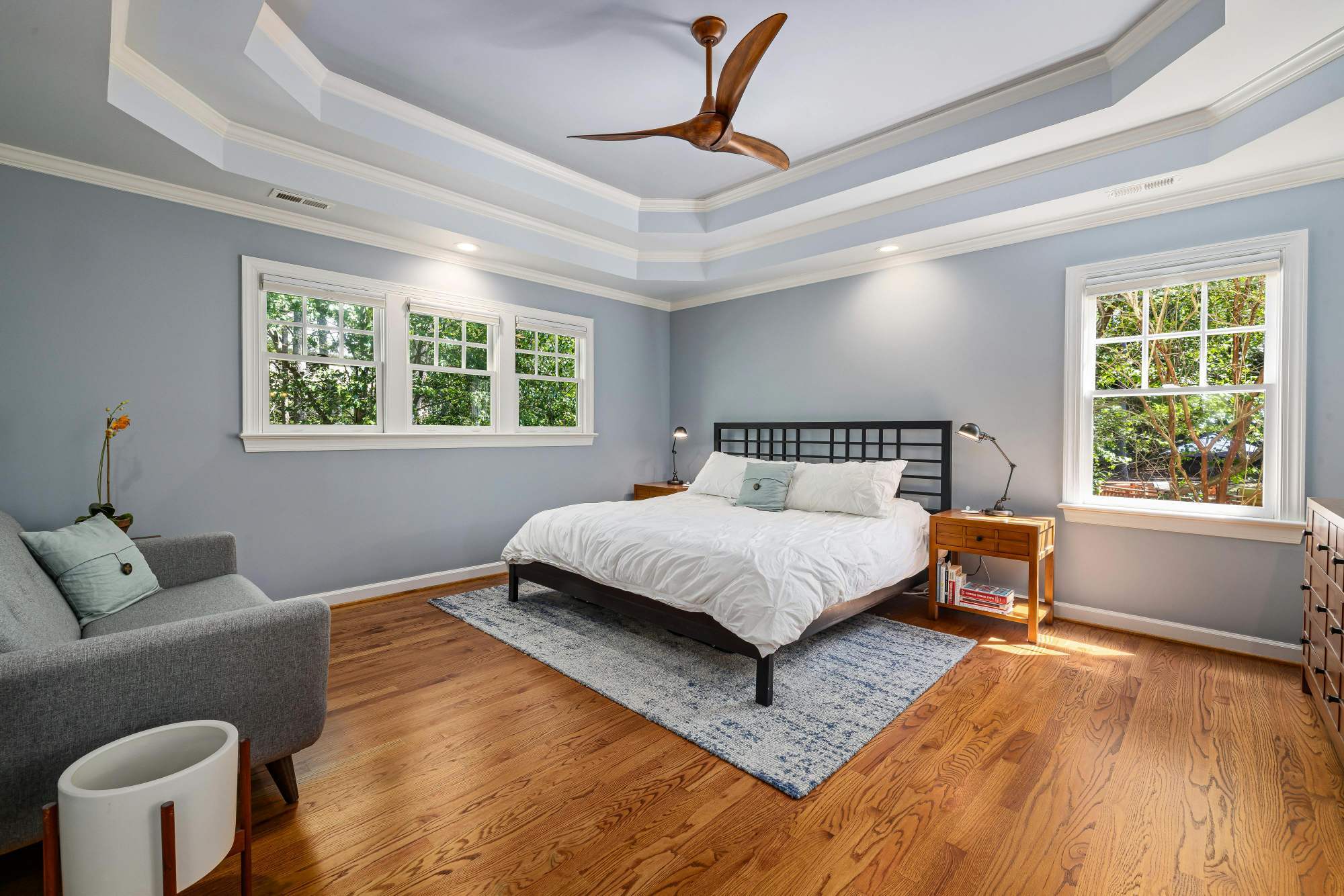 Primary bedroom with tray ceiling, hardwood floors, and abundant natural light in a home addition by Managed Renovations in Chevy Chase